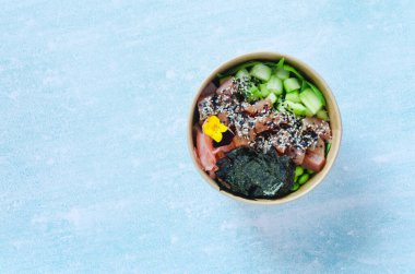 Tava kutusunun üst görüntüsü, siyah arka planda bir kase pirinç. Somon, avokado, soğan, mantar, brokoli ve susamlı pilav. Çin, Asya yemeği teslimatı. Tavalar için ambalaj. 