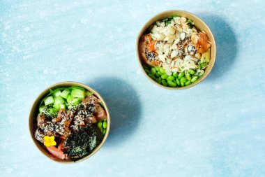 Tava kutusunun üst görüntüsü, siyah arka planda bir kase pirinç. Somon, avokado, soğan, mantar, brokoli ve susamlı pilav. Çin, Asya yemeği teslimatı. Tavalar için ambalaj. 