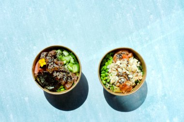 Tava kutusunun üst görüntüsü, siyah arka planda bir kase pirinç. Somon, avokado, soğan, mantar, brokoli ve susamlı pilav. Çin, Asya yemeği teslimatı. Tavalar için ambalaj. 