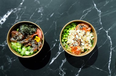 Tava kutusunun üst görüntüsü, siyah arka planda bir kase pirinç. Somon, avokado, soğan, mantar, brokoli ve susamlı pilav. Çin, Asya yemeği teslimatı. Tavalar için ambalaj. 