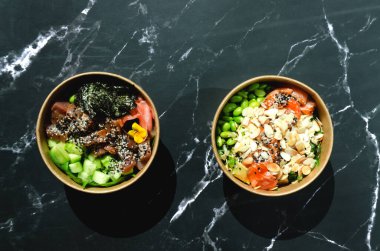 Tava kutusunun üst görüntüsü, siyah arka planda bir kase pirinç. Somon, avokado, soğan, mantar, brokoli ve susamlı pilav. Çin, Asya yemeği teslimatı. Tavalar için ambalaj. 