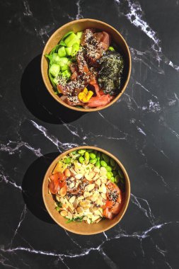 Tava kutusunun üst görüntüsü, siyah arka planda bir kase pirinç. Somon, avokado, soğan, mantar, brokoli ve susamlı pilav. Çin, Asya yemeği teslimatı. Tavalar için ambalaj. 