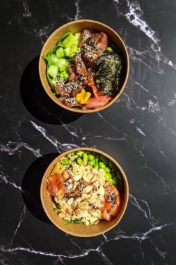 Tava kutusunun üst görüntüsü, siyah arka planda bir kase pirinç. Somon, avokado, soğan, mantar, brokoli ve susamlı pilav. Çin, Asya yemeği teslimatı. Tavalar için ambalaj. 