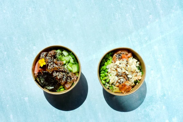 Tava kutusunun üst görüntüsü, siyah arka planda bir kase pirinç. Somon, avokado, soğan, mantar, brokoli ve susamlı pilav. Çin, Asya yemeği teslimatı. Tavalar için ambalaj. 