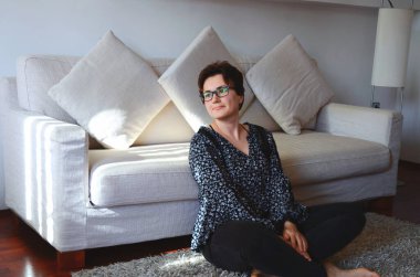 Mutlu iş kadını portresi. Günlük giysiler içinde. Rahat bir şekilde kanepede dizüstü bilgisayarla oturuyor. Kahve içiyorum. Evden çalışıyorum. İnternetten alışveriş