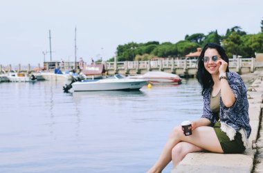 Yaşam Tarzı Portresi. Güzel, mutlu bir kadın sahilde yürüyor, dinleniyor, güneşli bir günde eğleniyor. Yaz. Kahve içiyorum. Adriyatik Denizi. Özgürlük