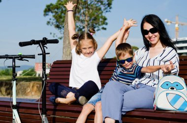 Mutlu aile hayatı ve tatil konsepti. Anne, küçük oğlan, kız oturuyor, eski şehirde, sokakta yürüyor. Güneşli bir yaz gününde gülüyorlar. Eğleniyorum.