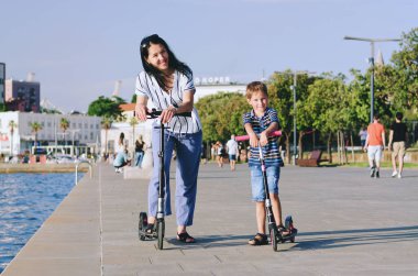 Happy family lifestyle and holiday concept. Mother, little boy, girl , riding scooters, walking in old city, street. Ice cream. Laughing on a summer sunny day. Having fun