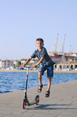 Mutlu aile hayatı ve tatil konsepti. Küçük çocuk mobilete biniyor, eski şehirde, sokakta yürüyor. Güneşli bir yaz gününde gülüyorlar. Eğleniyorum.