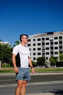 Genç, mutlu, sakallı adam, parkta oturan bir turist. Gülümsüyor, rahatlıyor. Yaz tatili. Güneş gözlüğü. Yaşam tarzı portresi. 