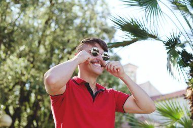Genç, mutlu, sakallı adam, parkta oturan bir turist. Gülümsüyor, rahatlıyor. Yaz tatili. Güneş gözlüğü. Yaşam tarzı portresi. 
