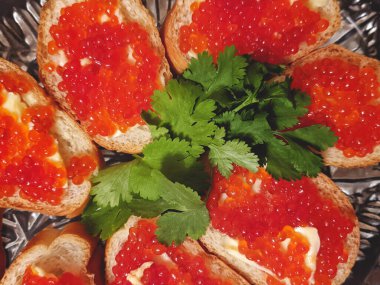 Sandwiches, canape with butter, herbs and red caviar on the festive table. Top view food. Black background