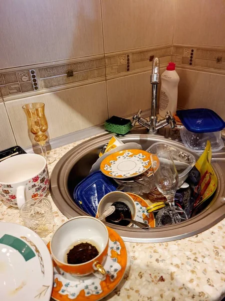 Dirty and unwashed dishes standing on the table in a kitchen at home. Cups of coffee, plates, spoons, forks are in the sink