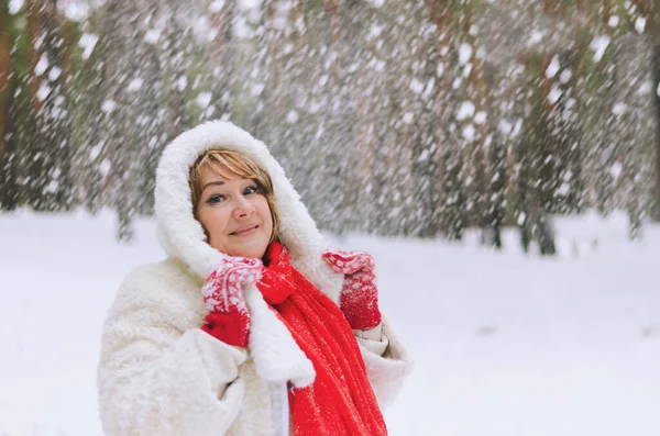 Portrait of funny old woman in jeans, white hat and jacket in snowy park, forest. Mother walking near snow covered pine trees.  Having fun. Family winter holidays. Christmas time
