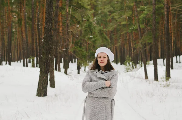 funny young woman in jeans, white hat and jacket in snowy park, forest. Girl walking near snow covered pine trees.  Having fun. Family winter holidays.