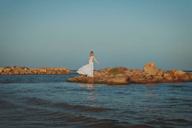 Beautiful young elegant pregnant blond woman in a blue hat walks on the beach, seashore at sunset. Azov sea. Motherhood.