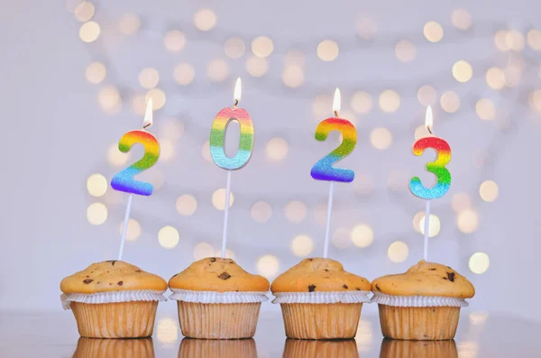 Christmas sweet cupcakes and candles in form of numbers 2023. White background with bokeh. New year celebration. Food.