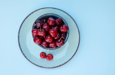 Mavi tabakta kırmızı kirazlı üst manzara. Vegan, yaz yemeği konsepti. Diyet