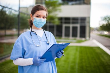 Steteskoplu ve cerrahi koruyucu maskeli modern tıp doktoru kadın klinik girişinin önünde, yeni hastaları sağlık merkezine kabul eden hoş, hoş bir bayan.