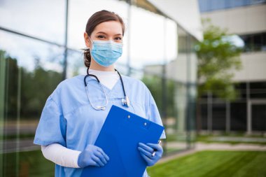 Hastane ya da kliniğin önünde duran genç, dost canlısı beyaz kadın doktor, acil ambulans girişinin önünde ilk müdahale ekibi, üniformalı kadın doktor portresi.