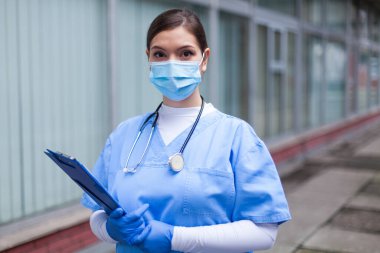 Endişeli kadın doktor portresi, klinik ya da hastane binasının önünde duruyor, uzun gece vardiyasından bitap düşmüş, endişeli bir şekilde kameraya bakıyor, güvensiz bir geleceği var.