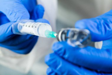 Ampul şişesinde iğne olan makro yakın çekim şırınga, aşı ekipmanı taşıyan mavi lateks eldivenler, Coronavirus bulaşıcı hastalıklardan korunmak için COVID-19 bağışıklık prosedürü