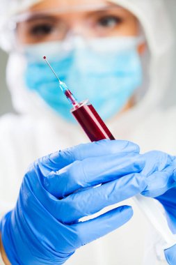 Kadın bilim adamı ya da tıp doktoru elinde kanla dolu bir şırınga, seroloji laboratuvarı test prosedürü, COVID-19 iyileşen hasta trombositi zengin plazma nakli terapisi, virüse karşı bağışıklık.
