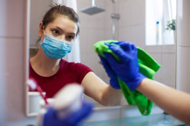 Yüz maskesi takan beyaz bir kadın ve koruyucu eldivenler takıyor. Antibakteriyel spreyle tuvaleti dezenfekte ediyor. Coronavirus COVID-19 virüs salgını sırasında koruyucu önlemler artıyor.