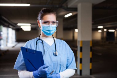 PPE maskeli kadın doktor ya da hemşire ellerinde tıbbi form panosu, test ya da aşı merkezleri Coronavirus COVID-19 salgını sırasında ciddi bir kurtarma çalışanı portresi tutuyordu.