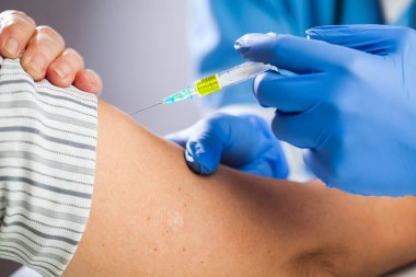 Covid-19 aşı, doktor elinde şırınga tutan mavi eldivenler, hastanede veya klinikte yaşlı bir kadın hastaya iğne yapıyor, Coronavirus hastalığının önlenmesi, koruyucu iğne, tedavi