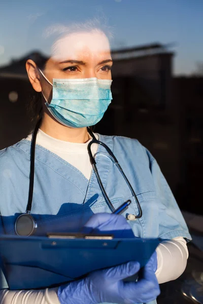 Młody Zaniepokojony Lekarz Noszący Maskę Ochronną Patrzący Przez Okno Szpitala — Zdjęcie stockowe