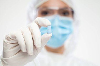 PPE kişisel koruyucu ekipman, tulum, yüz maskesi, eldiven, mavi hap, seçici odaklanma, hasta tedavisi ve hastalık için ilaç, reçeteli ilaç konseptörü kullanan İngiliz kadın eczacı.
