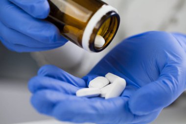 Closeup of medical worker or pharmacist hands wearing blue latex protective gloves,pouring white medicine pills on palm of hand,Coronavirus therapy treatment illustration,cure for COVID-19 new variant