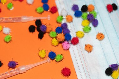 Vaduz, Lihtenştayn, 17 Aralık 2021 Turuncu arka planda virüs parçacıkları ve şırıngalarla tıbbi yüz maskeleri