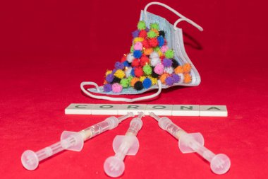 Vaduz, Lihtenştayn, 17 Aralık 2021 Virüs parçacığı varyasyonları şırıngalı tıbbi yüz maskesi ve yazılı Corona kelimesi