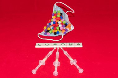 Vaduz, Lihtenştayn, 17 Aralık 2021 Virüs parçacığı varyasyonları şırıngalı tıbbi yüz maskesi ve yazılı Corona kelimesi