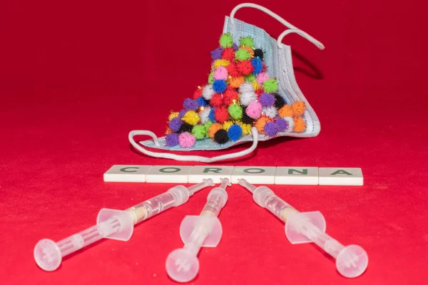 Vaduz, Lihtenştayn, 17 Aralık 2021 Virüs parçacığı varyasyonları şırıngalı tıbbi yüz maskesi ve yazılı Corona kelimesi