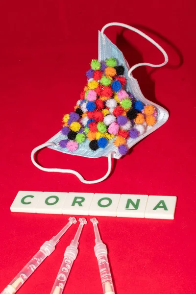 Vaduz, Lihtenştayn, 17 Aralık 2021 Virüs parçacığı varyasyonları şırıngalı tıbbi yüz maskesi ve yazılı Corona kelimesi