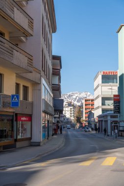 Davos, İsviçre, 23 Mart 2022 Güneşli bir günde şehirde binaları ve dükkanları olan bir cadde boyunca bakın.