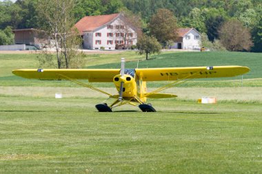 Lommis, İsviçre, 11 Mayıs 2022 Piper PA18-150 Super Cub pervaneli uçak küçük bir havaalanındaki çimlerin üzerinde taksicilik yapıyor.,