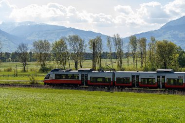Nendeln, Liechtenstein, April 28, 2022 Local austrian train is passing over a green meadow on a sunny day