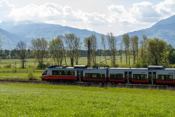 Nendeln, Liechtenstein, April 28, 2022 Local austrian train is passing over a green meadow on a sunny day