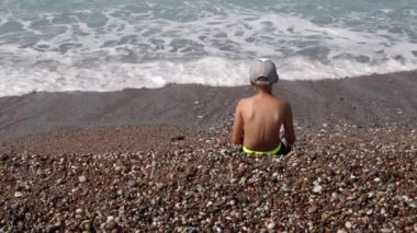 Bir çocuk deniz kenarında oturur ve taş atar. Tam HD görüntüler