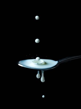 Siyah arka planda sütlü kaşık ve bir damla süt..