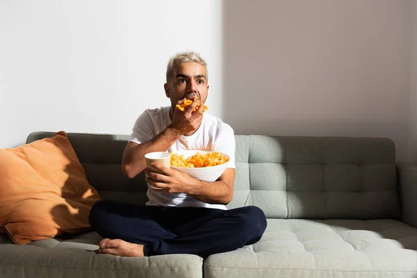 İspanyol adam televizyon izlerken kanepede şeker yiyor. Sağlıksız beslenme ve kötü alışkanlıklar.