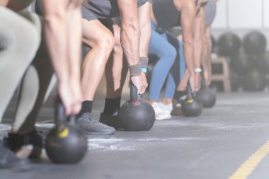 Bir grup yüzsüz sporcu, çapraz eğitim merkezinde kettlebell ile çalışıyor.