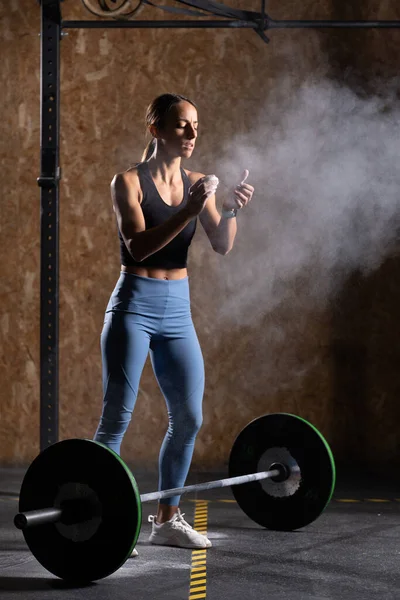 Concentrated fit woman clapping hands with chalk before lifting a heavy barbell.