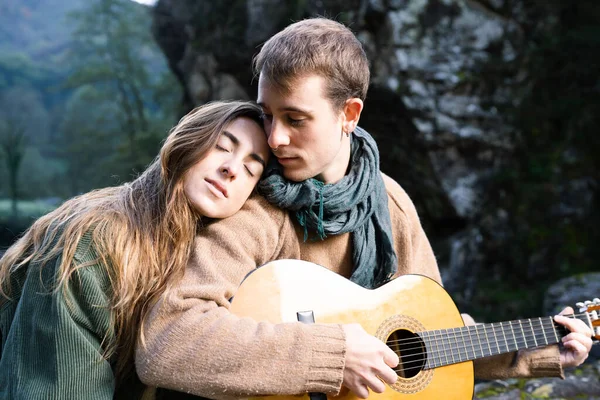 Romantic young couple playing guitar outdoors in a park