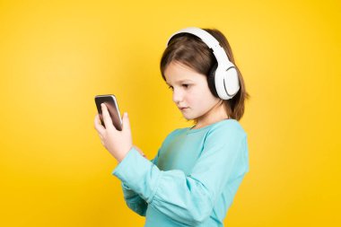 Kulaklık takan, telefonu kullanan ve müziği seçen küçük kız..