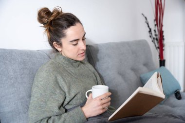 Bir fincan kahve içerken kitap okuyan ve ders çalışan genç bir kadın.